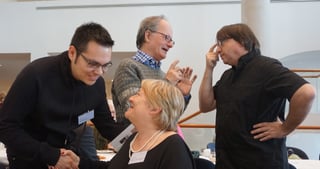 Four participants laughing and talking, one man touching his forehead