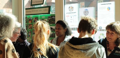 Visitors at exhibition stands with posters in front of the windows