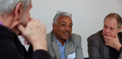 A laureate speaking at a round table while others listen