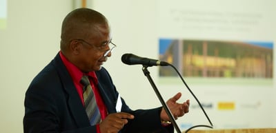 Man in a red shirt speaking at a microphone stand in front of a projected slide