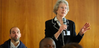 Older woman with glasses speaking into a microphone and gesturing