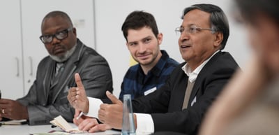 Three men at a round table, one gesturing as he speaks