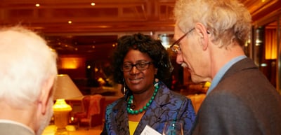 Woman with glasses and a green necklace talking with an older man in a warmly lit room