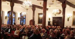 Audience in the historic hall of the Historisches Kaufhaus with chandeliers and dark wooden columns