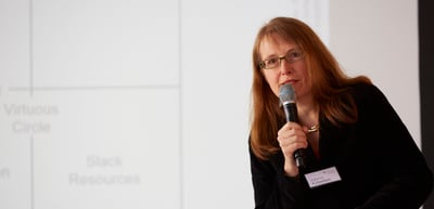 Woman with glasses speaking into a microphone in front of a projected diagram