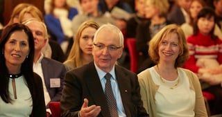 Audience in the front row, an older man in a suit gesturing while he speaks