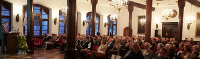 Opening ceremony in a historic hall with chandeliers and a full audience
