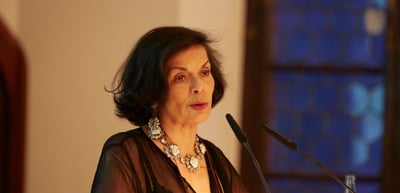 Woman with a large necklace speaking at a lectern microphone