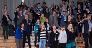 Young people and laureates on a staircase stretch their arms towards the camera