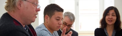 Teenage boy speaking and gesturing at a round table with adults