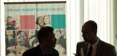 Two men talking in front of a roll-up banner of the UWC Robert Bosch College
