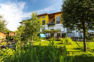 Garden with trees in front of a yellow residential building in Freiburg-Rieselfeld
