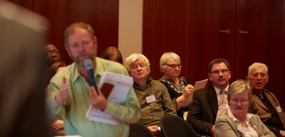 Man in the audience speaking into a microphone while holding papers