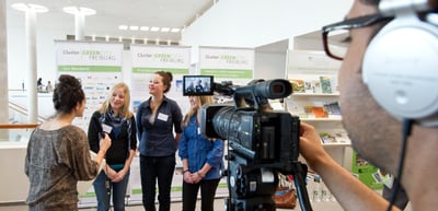 Camera operator filming an interview with three young women in an exhibition room