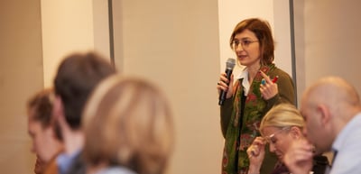 Woman with glasses standing in the audience and speaking into a microphone