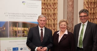 Two men and a woman in front of a banner of the 6th International Convention of Environmental Laureates, Freiburg, Germany, 9-12 March 2017