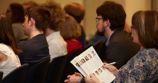 Audience listening, a woman holding a programme with portrait photos