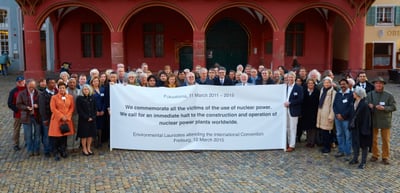 Environmental laureates in front of the red Historisches Kaufhaus in Freiburg holding a banner about the victims of nuclear power