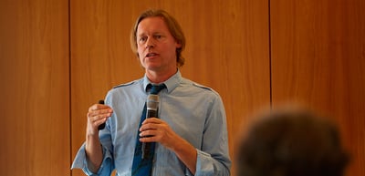 Man in a blue shirt speaking into a handheld microphone