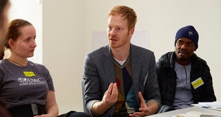 Young man gesturing while he talks to a young woman and a young man at a table