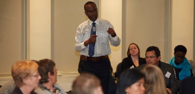 Man in a shirt and tie speaking to a seated audience