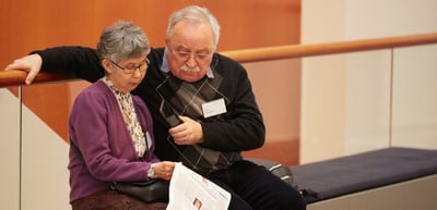 Older woman and older man sitting on a bench reading papers