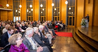 Audience in a wood-panelled hall listening to a speaker at a lectern