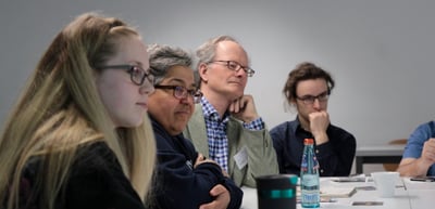Round table group of students and older participants listening