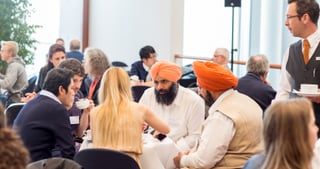 Participants at breakfast tables in a bright foyer, two men wearing orange turbans