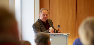 Man speaking at a lectern in a room with wood panelling