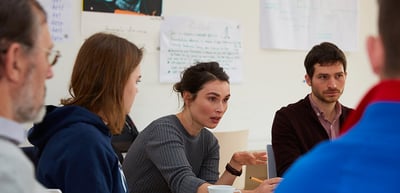 Students and a laureate talking at a round table in front of flip charts