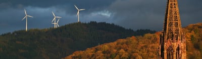 Spire of Freiburg Cathedral in front of a wooded hill with wind turbines