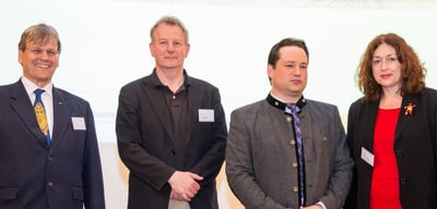 Four people standing side by side in front of a white wall