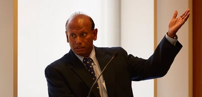 Man in a suit speaking and pointing upwards with his raised hand