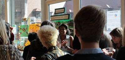 Crowd of visitors at the exhibition stands in a room with posters at the windows