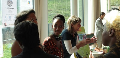 Young women talking with a woman holding a brochure at an exhibition stand
