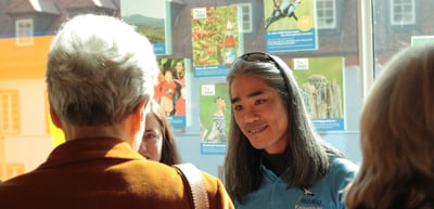 Woman with glasses on her head smiling in conversation in front of colourful posters