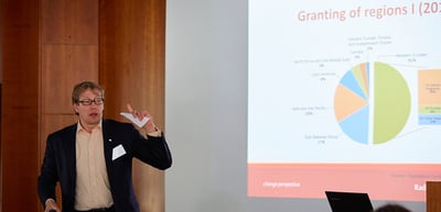 Man presenting in front of a projected pie chart with the title "Granting of regions"