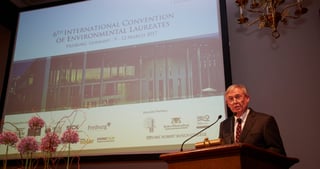 Speaker at a lectern next to a screen reading "6th International Convention of Environmental Laureates, Freiburg, Germany, 9-12 March 2017"