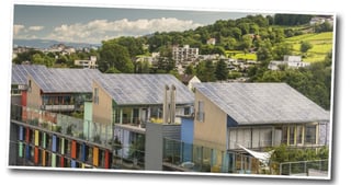 Buildings with solar roofs and colourful balconies in front of green hills