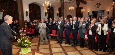 Speaker at a lectern and a standing audience applauding in the historic hall of the Historisches Kaufhaus