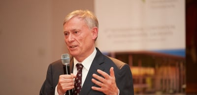 Man with grey hair speaking into a handheld microphone and gesturing