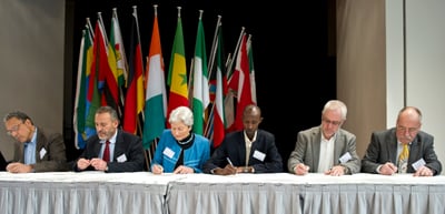 Panel of six people seated at a table in front of national flags