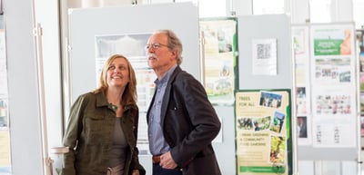 Woman and man smiling in front of exhibition boards with project posters