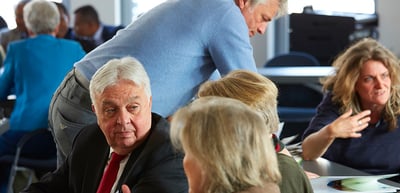 Participants in a group discussion around a table, a woman gesturing