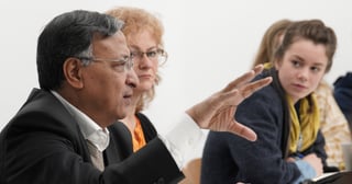 A laureate gesturing as he speaks at a round table while a young woman listens