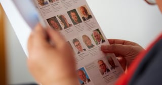 Hands holding a printed list with portrait photos of the participants