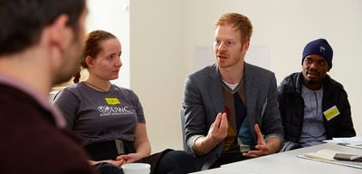 A man in a grey jacket speaking at a round table with young participants