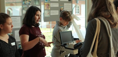 Young people at an exhibition stand with a microscope and a laptop