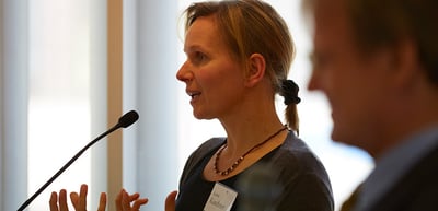 Woman speaking into a microphone and gesturing with both hands
